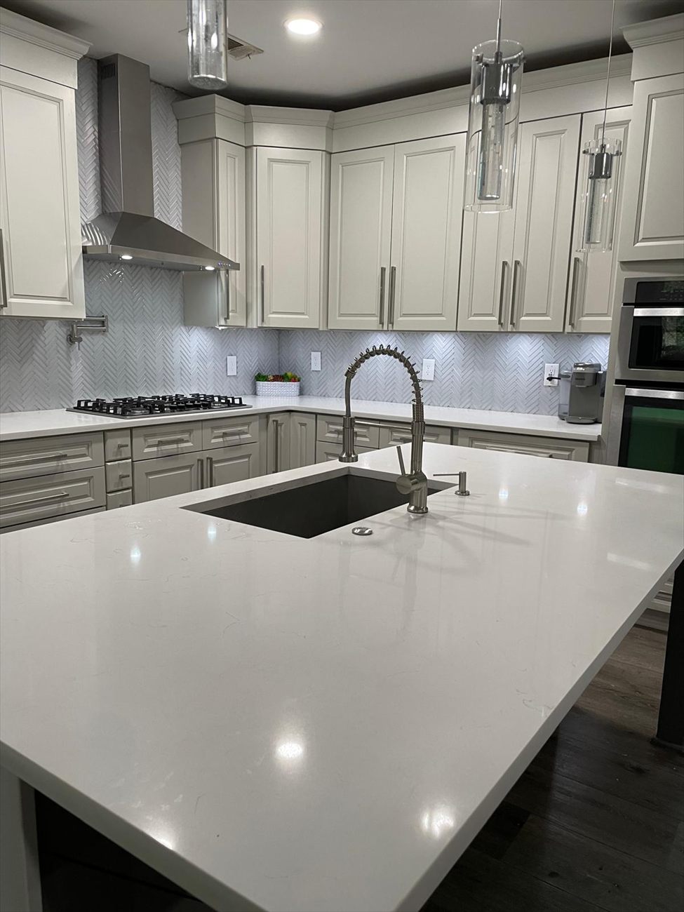 Renovated kitchen with a quartz island, glass pendant lights and a herringbone tile backsplash