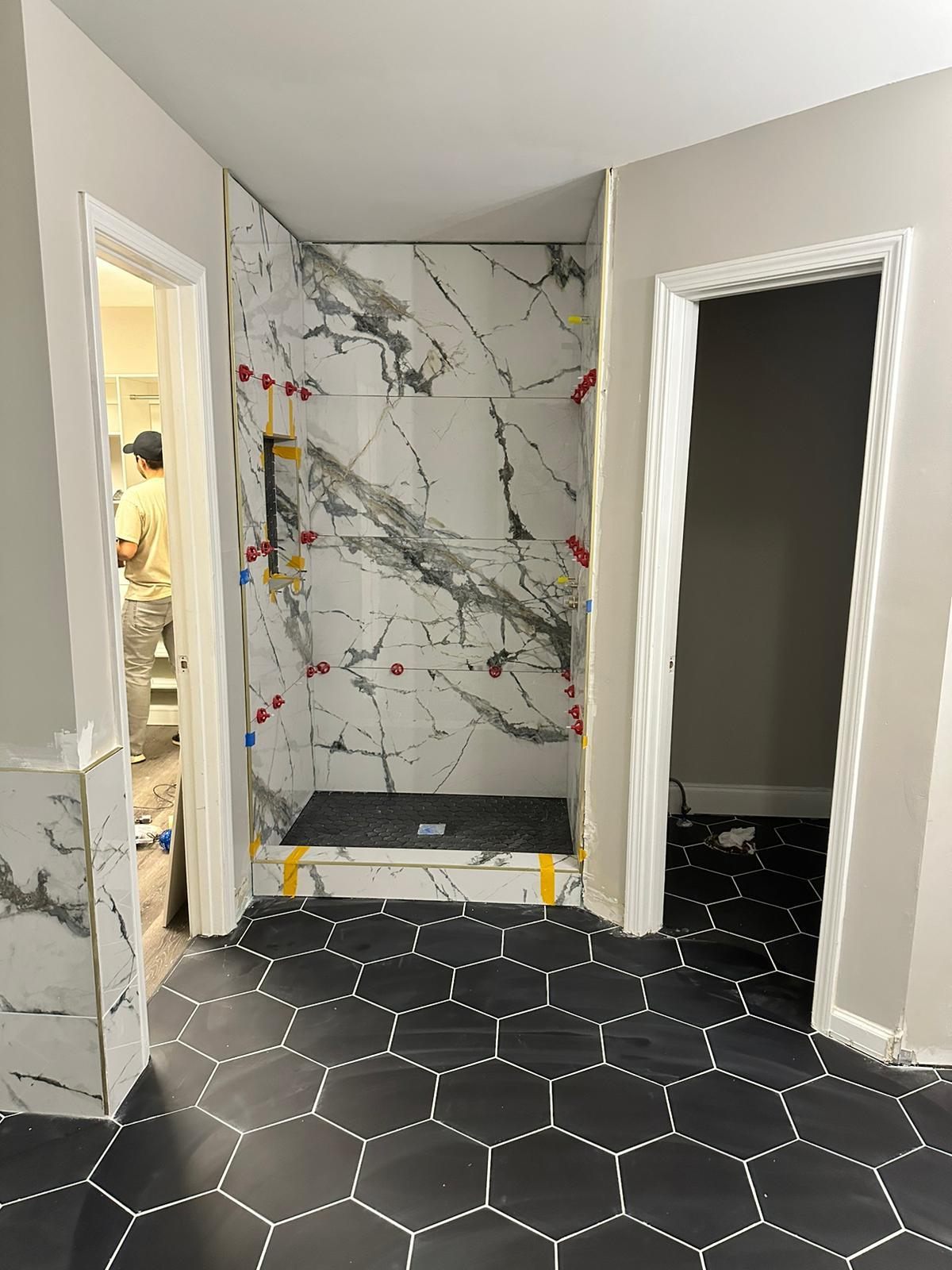 The same shower during construction, marble panels set but ungrouted, protective film and spacer clips still on, glass door not yet installed
