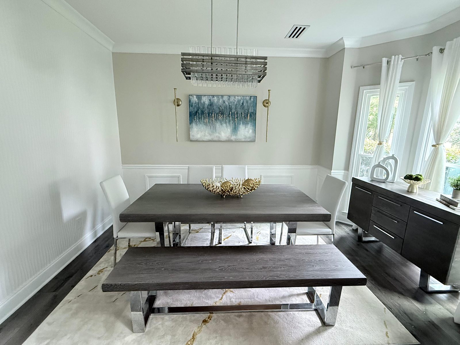 Dining room after renovation with fresh wainscoting, brass sconces, artwork and a linear crystal chandelier