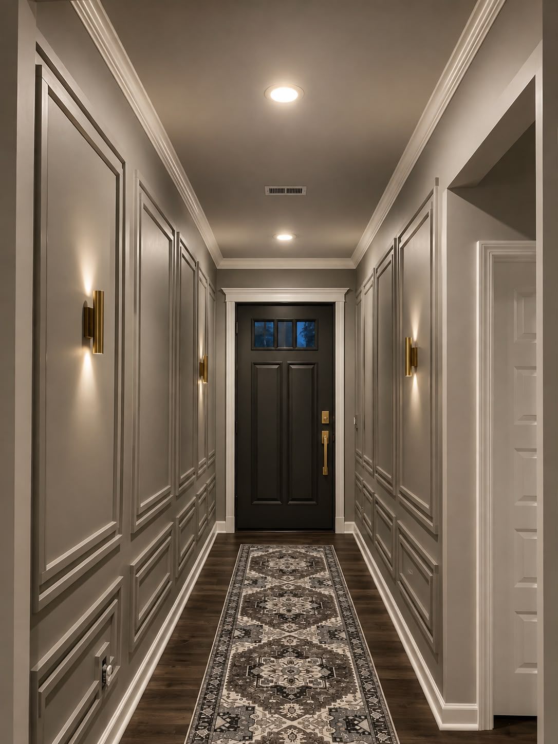 Renovated entry hallway with picture frame wall molding, brass sconces and dark hardwood flooring