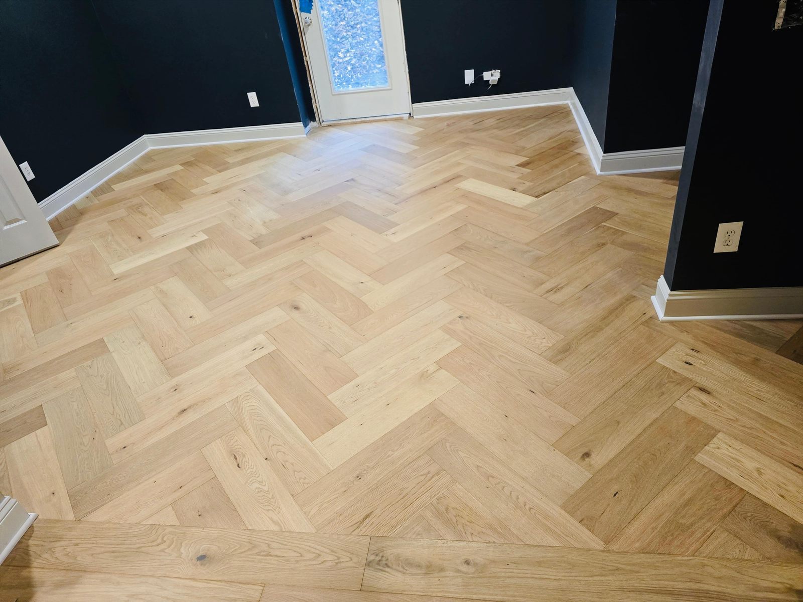 White oak herringbone floor installed against deep navy walls and white baseboard
