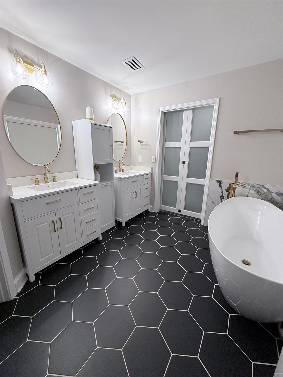 Primary bathroom with a double vanity, freestanding tub with a floor mount filler and frosted glass pocket doors